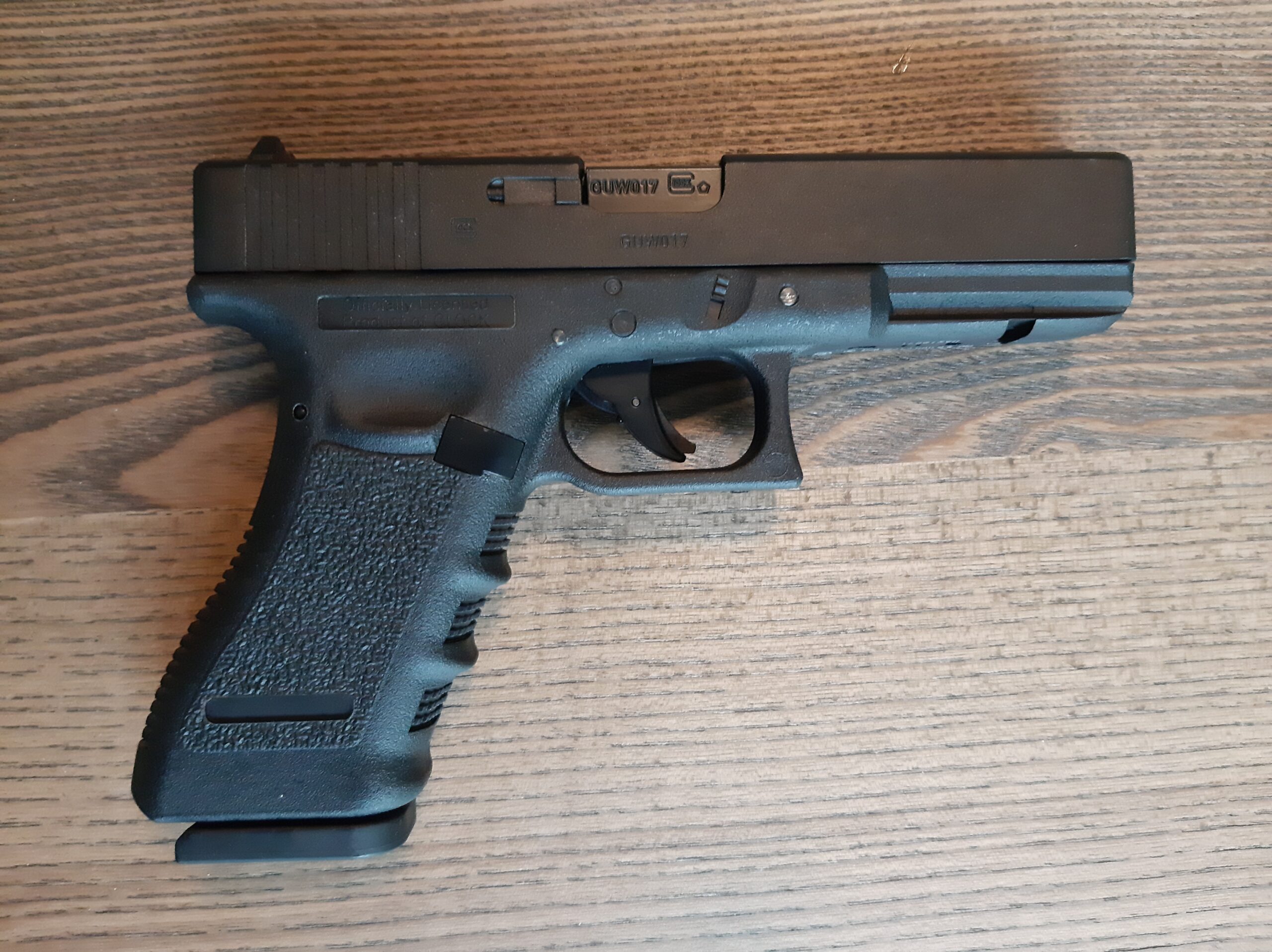 Umarex Glock17 ilmapistooli | Suomen Erämetsästys Close-up side view of a black semi-automatic pistol on a wooden surface, showing the slide and trigger area clearly.